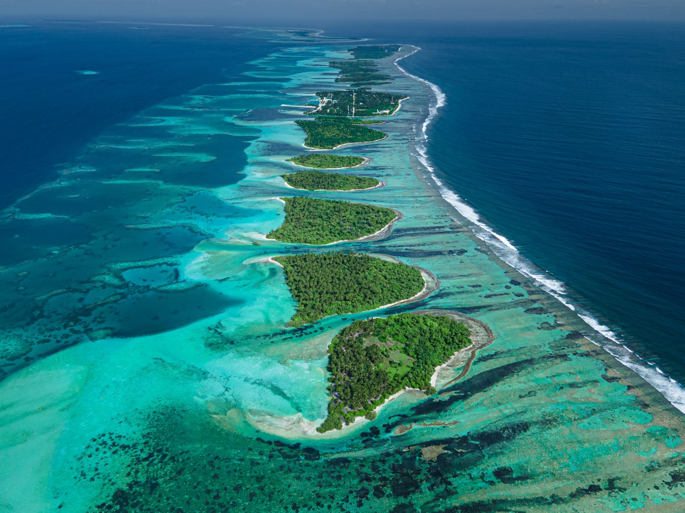 Aerial view of a Maldives atoll with green islands in vivid blue water
