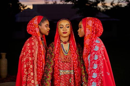 Free Three women in colorful traditional attire standing against a sunset backdrop, showcasing cultural fashion and unity. Stock Photo