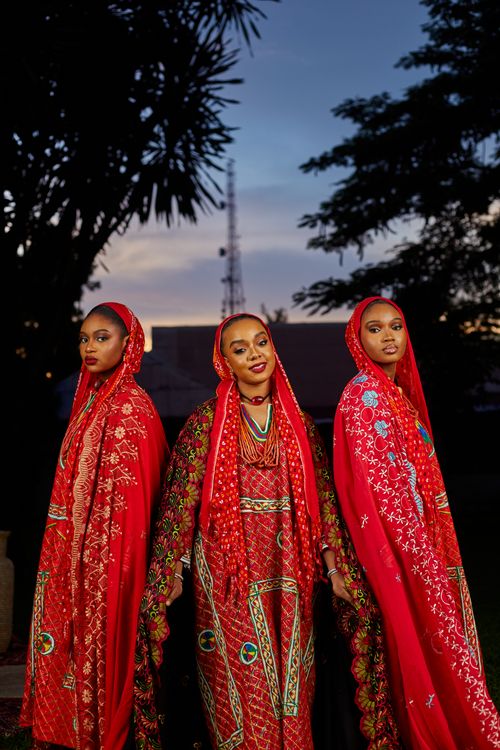 Free Three women in traditional red attire pose outdoors at dusk, showcasing cultural fashion. Stock Photo
