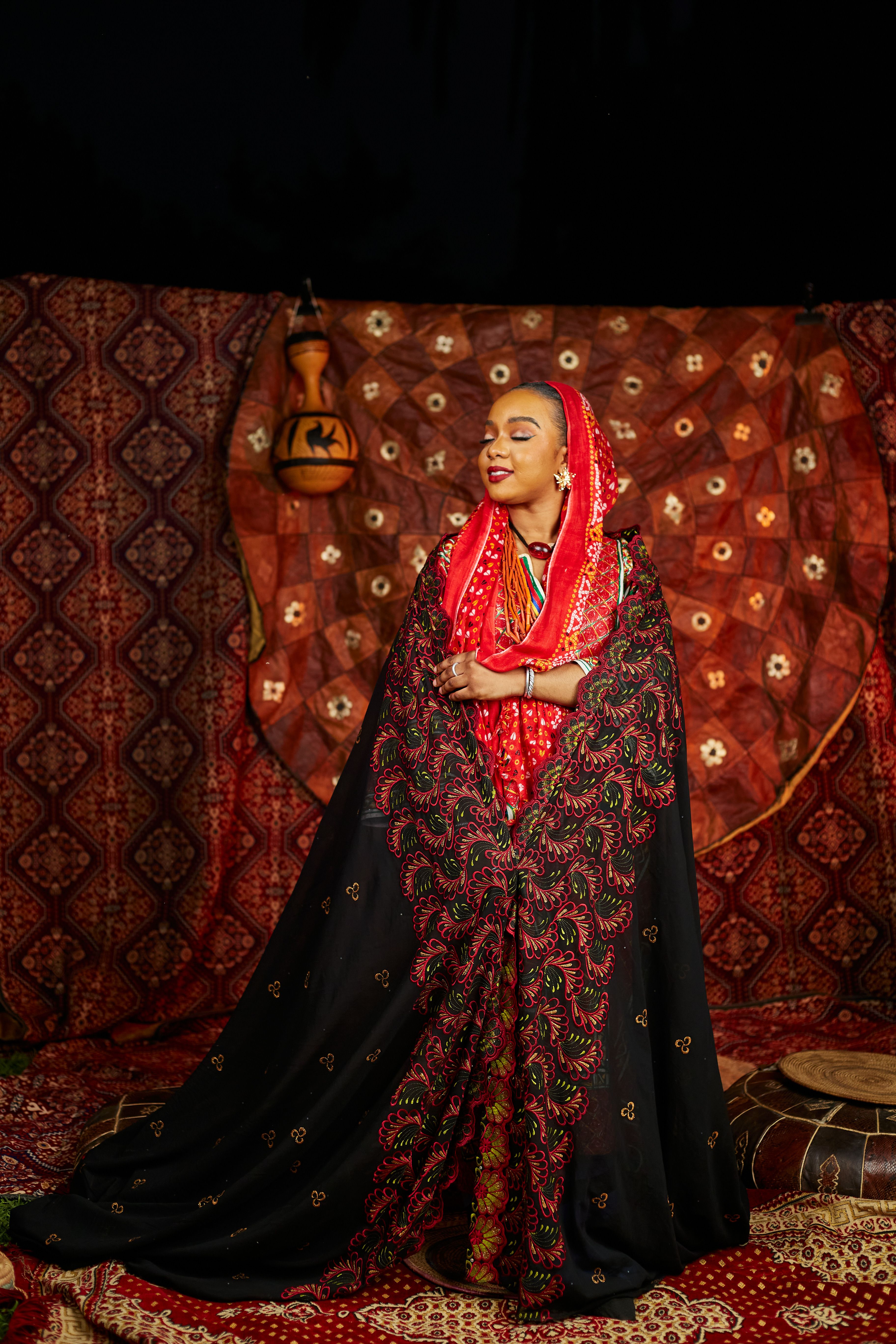Woman in traditional attire standing in front of ornate backdrop indoors.