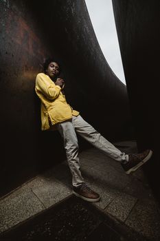 A fashionable man in a yellow shirt poses confidently in Berlin's unique urban landscape, highlighting modern architecture.