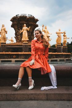A woman in a red polka dot dress sits by golden statues at a famous landmark.