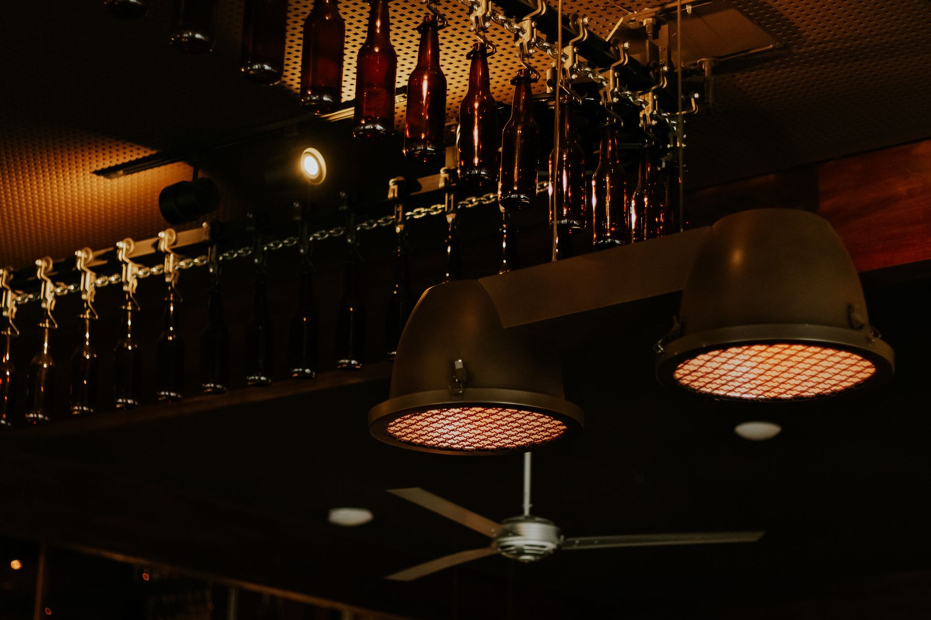 Industrial style ceiling lights and bottles create a moody ambiance in a São Paulo bar interior.