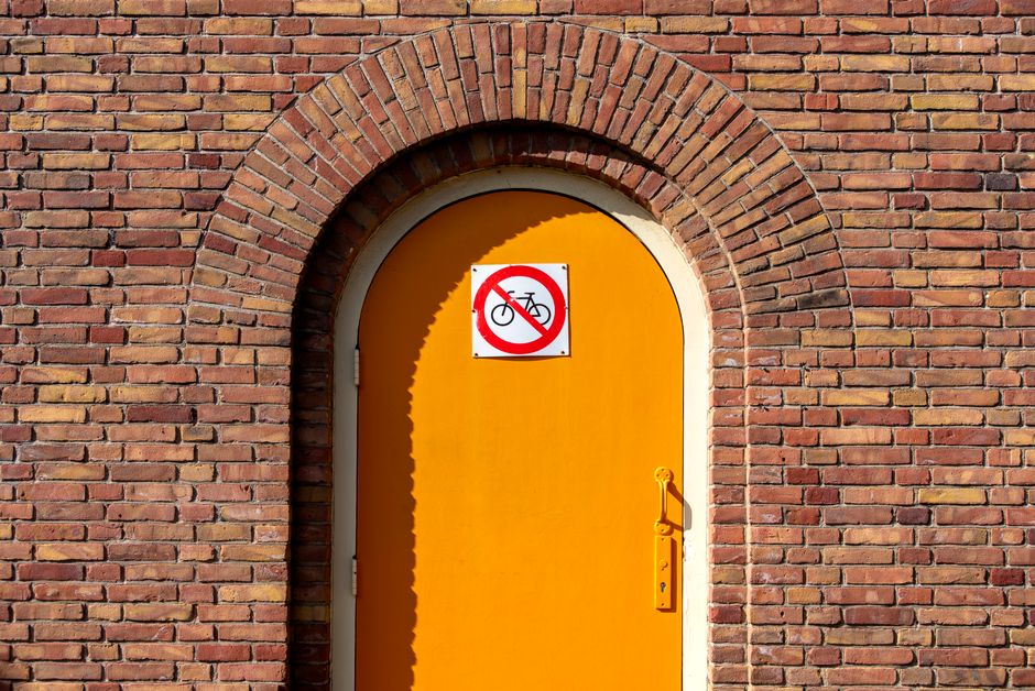 A vibrant orange door with a no bicycles sign against a brick wall, capturing a bold architectural statement.