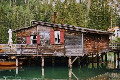 Weathered timber boathouse standing on stilts over a green alpine lake, pine forest behind — photo by eberhard grossgasteiger on Pexels