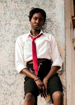 Stylish woman with a red tie posing confidently against a textured wall.