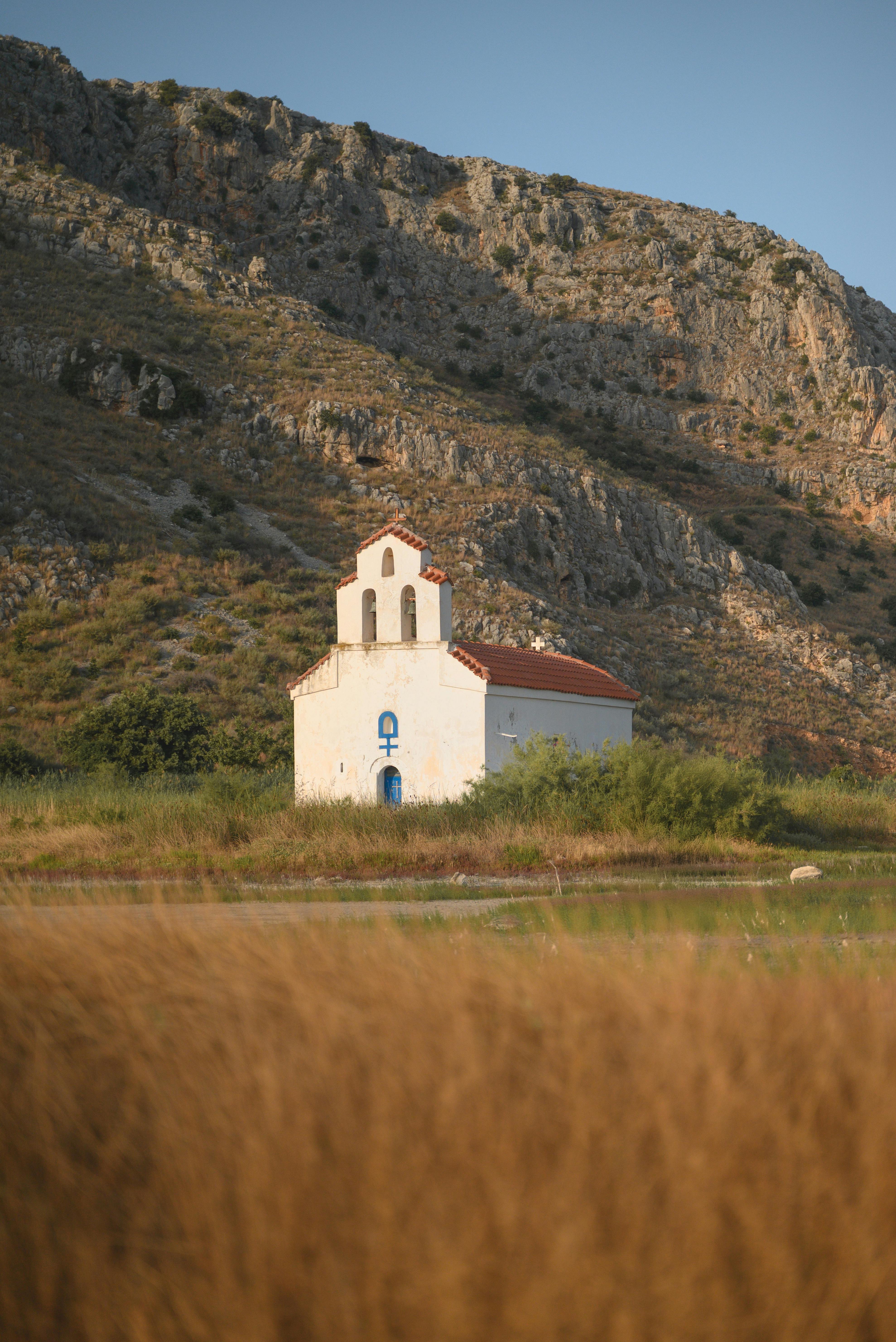 A picturesque white church set against a rugged mountain backdrop during sunset, conveying tranquility.