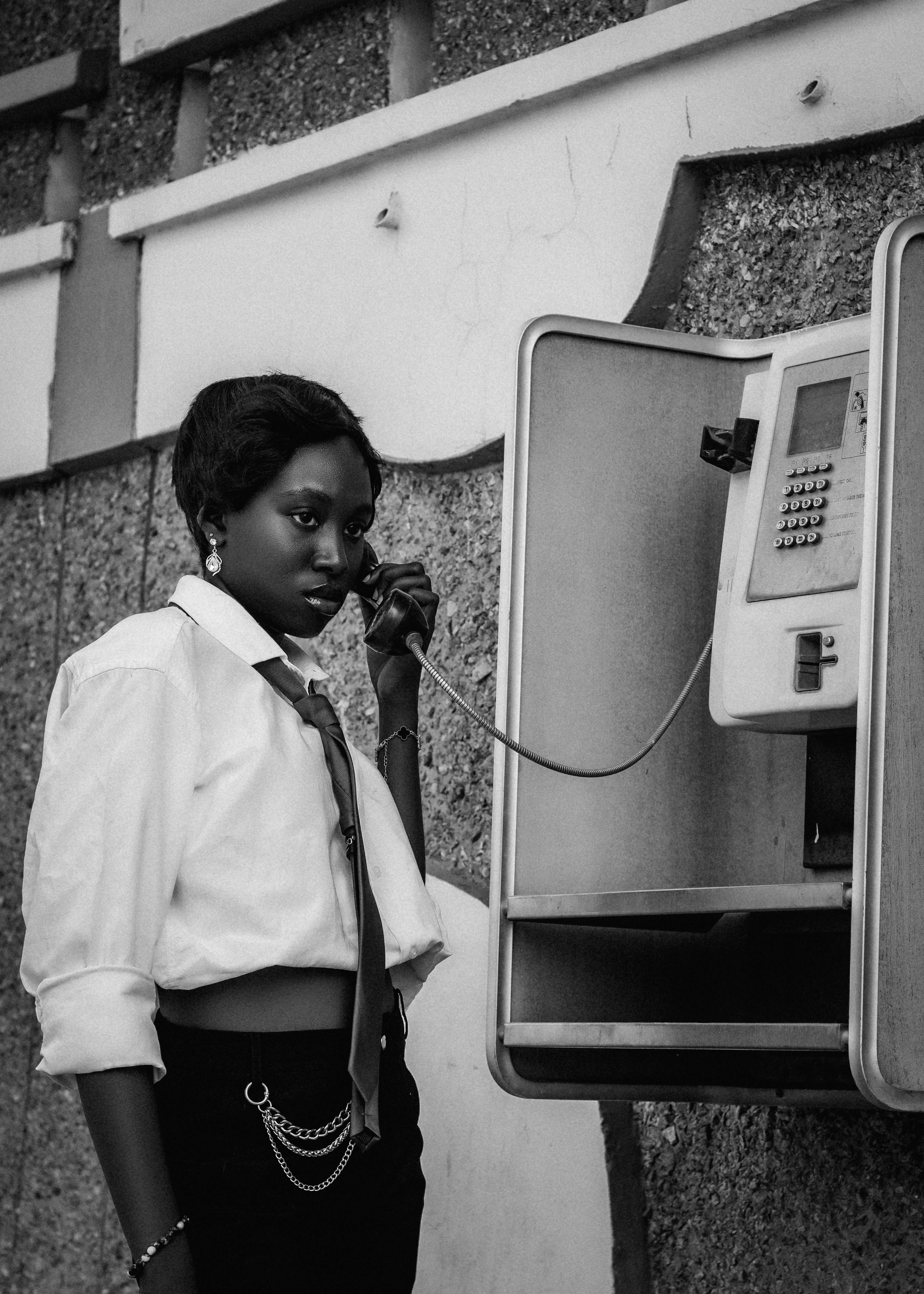 Artistic black and white photo of a woman using a public phone booth, evokes nostalgia.