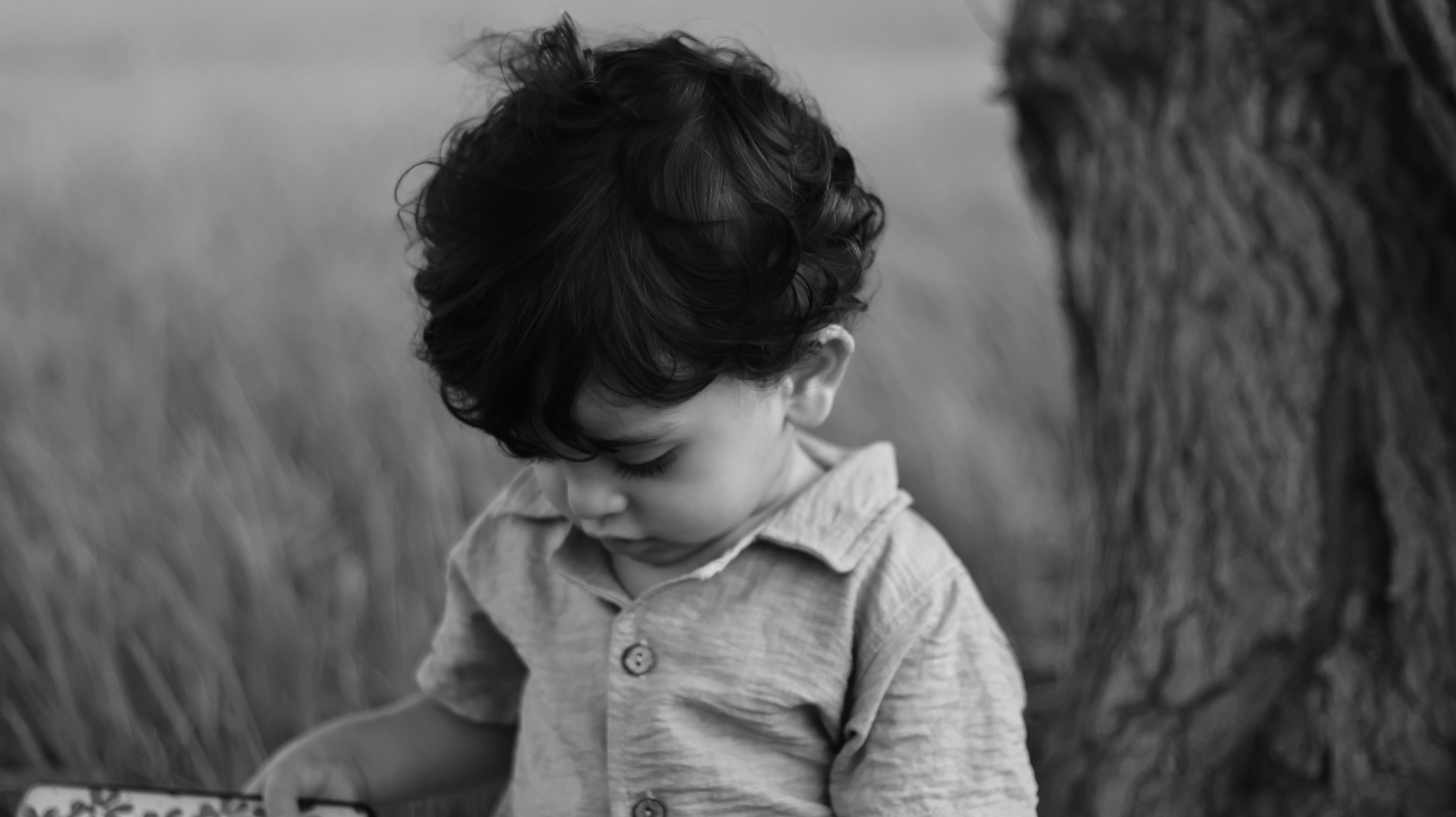 Black and white photo of a child standing by a tree, looking down.