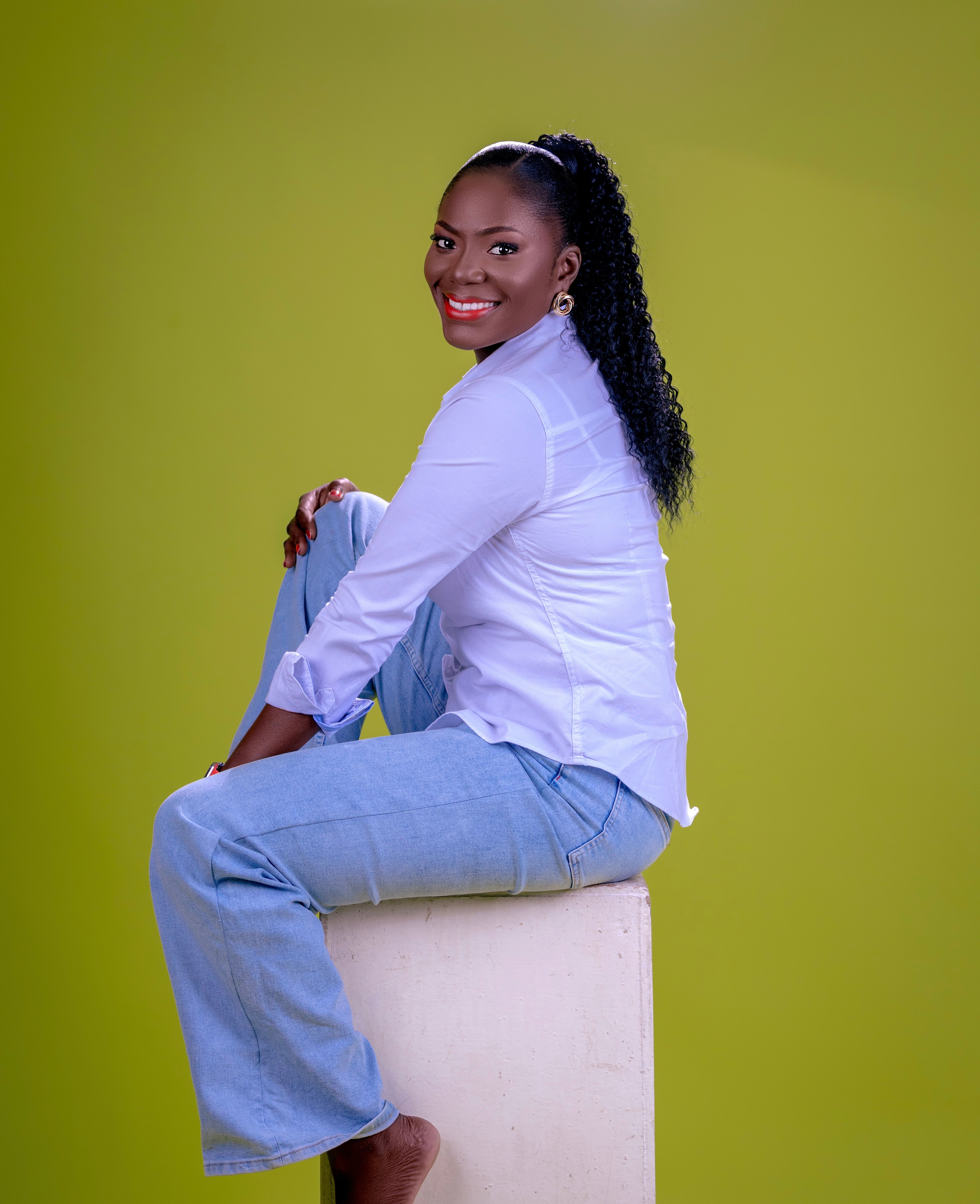 Studio photograph of a smiling woman sitting on a block with a vibrant background, Ghana.