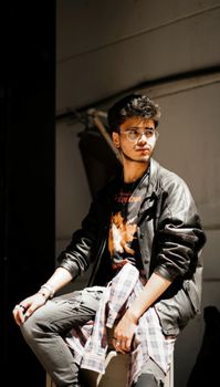 Fashionable young adult in urban setting wearing sunglasses and leather jacket.