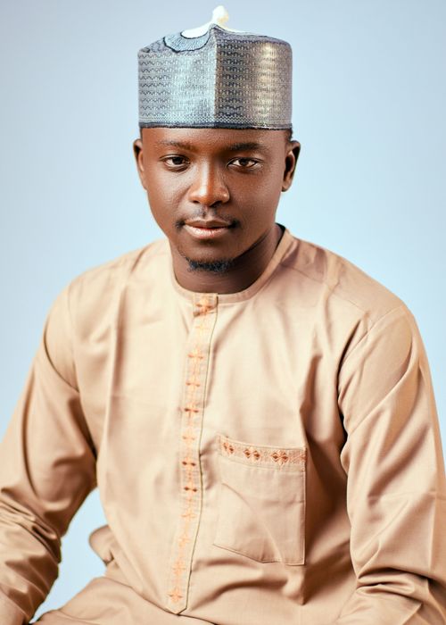 Free A close-up portrait of a young man wearing traditional African clothing and a cap, against a neutral background. Stock Photo