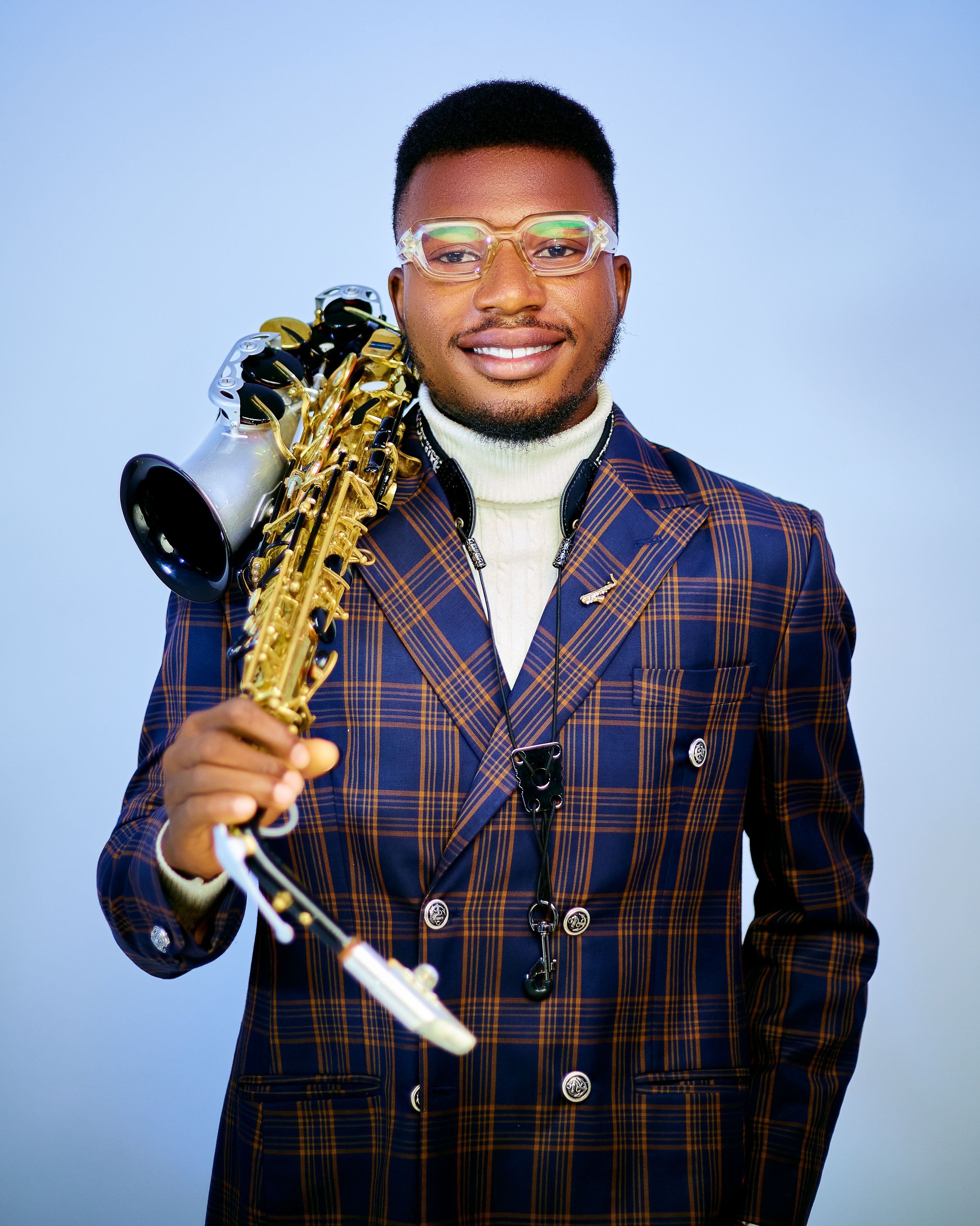 Fashionable man with saxophone in a plaid suit, posing confidently.