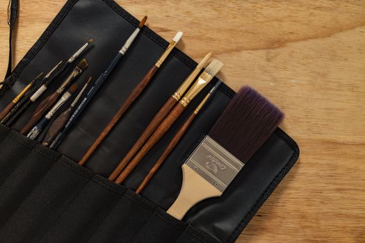 A variety of paintbrushes neatly arranged in a black fabric holder on a wooden surface.