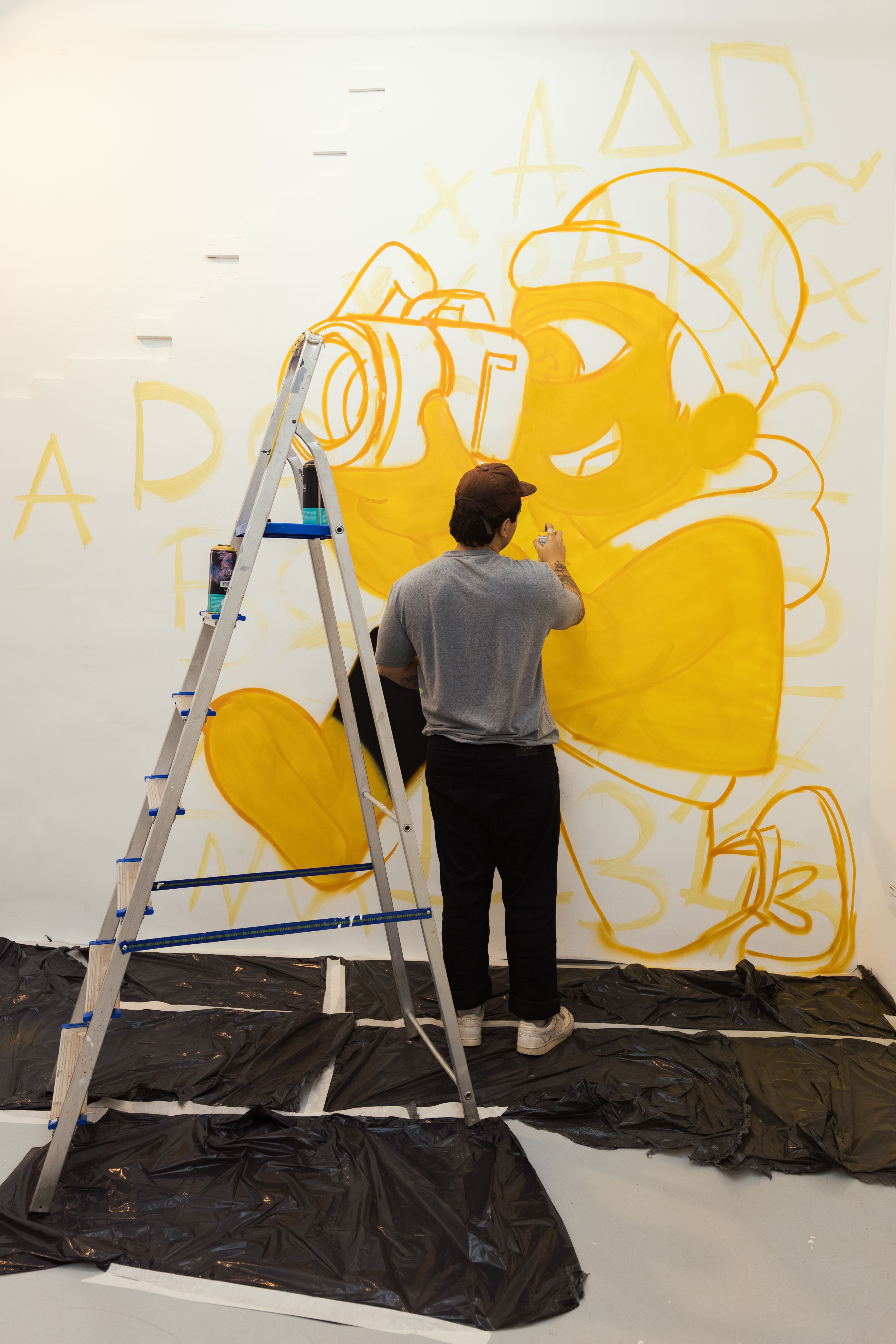 Artist creating a vibrant mural on a wall using yellow paint and a ladder.