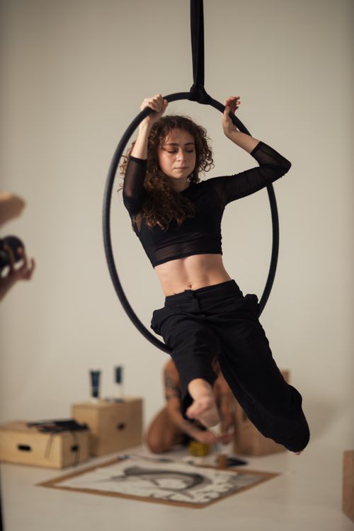 Free Woman performs aerial hoop acrobatics in an indoor studio setting, showcasing flexibility and strength. Stock Photo