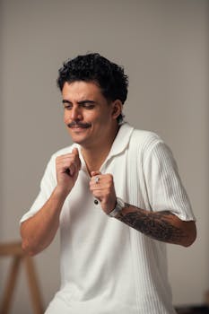 Young man in a white shirt smiling and enjoying a peaceful moment indoors with a neutral background.