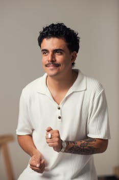 Casual portrait of a young man with tattoos, smiling in a white polo shirt against a simple background.
