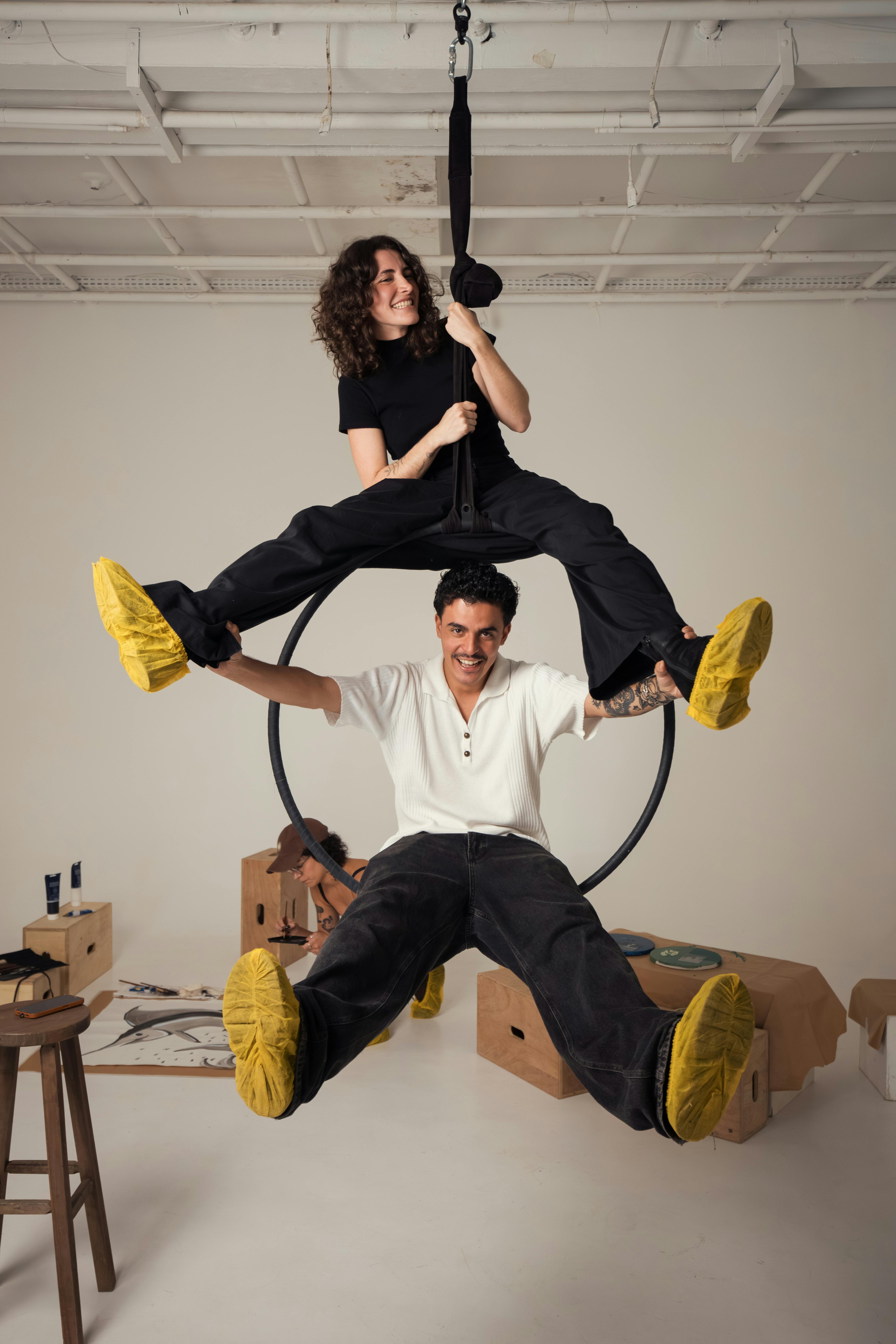 Two adults creatively pose on a suspended aerial ring in a studio, showcasing balance and coordination.