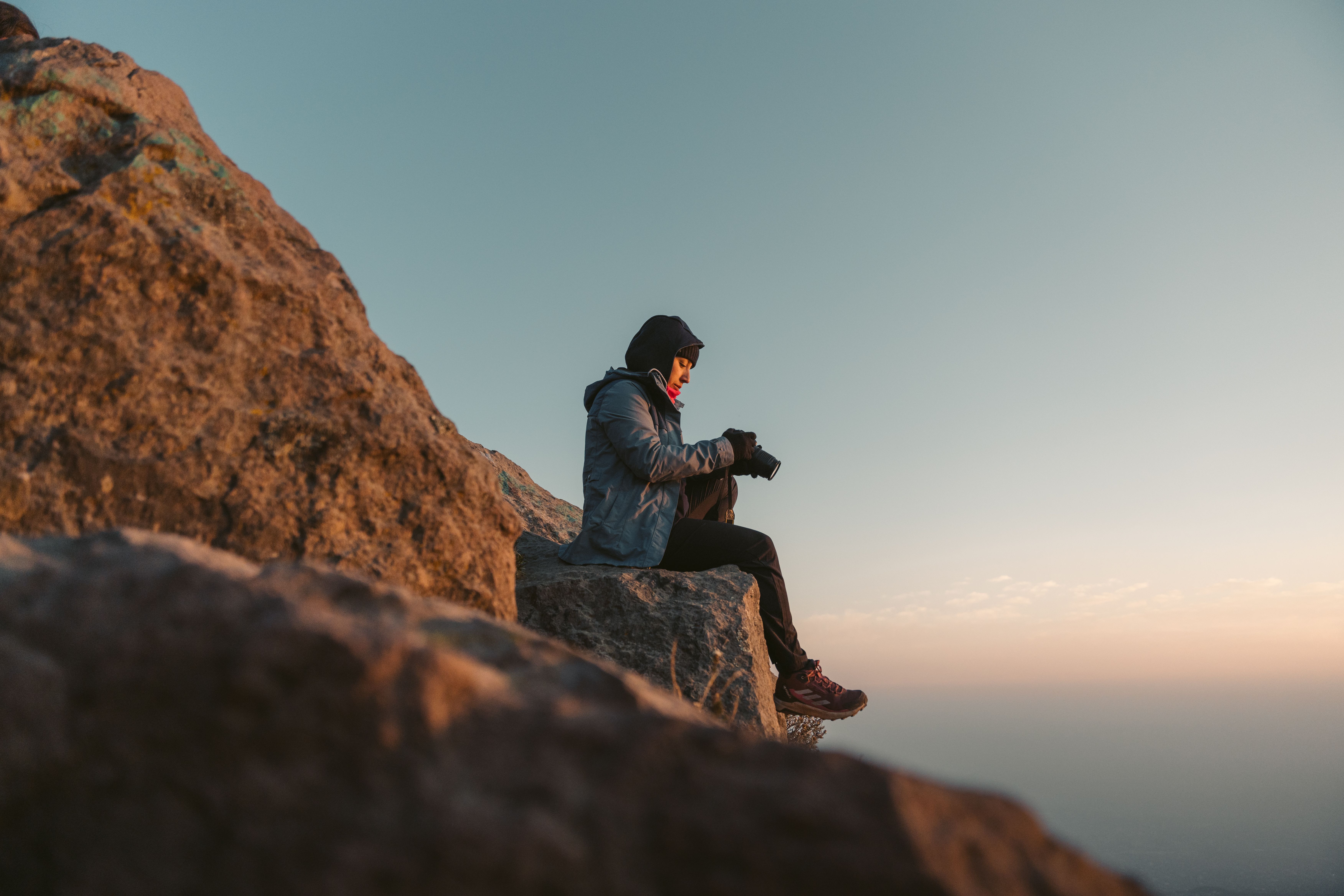Person hiking alone on a mountain trail at sunrise, looking contemplative