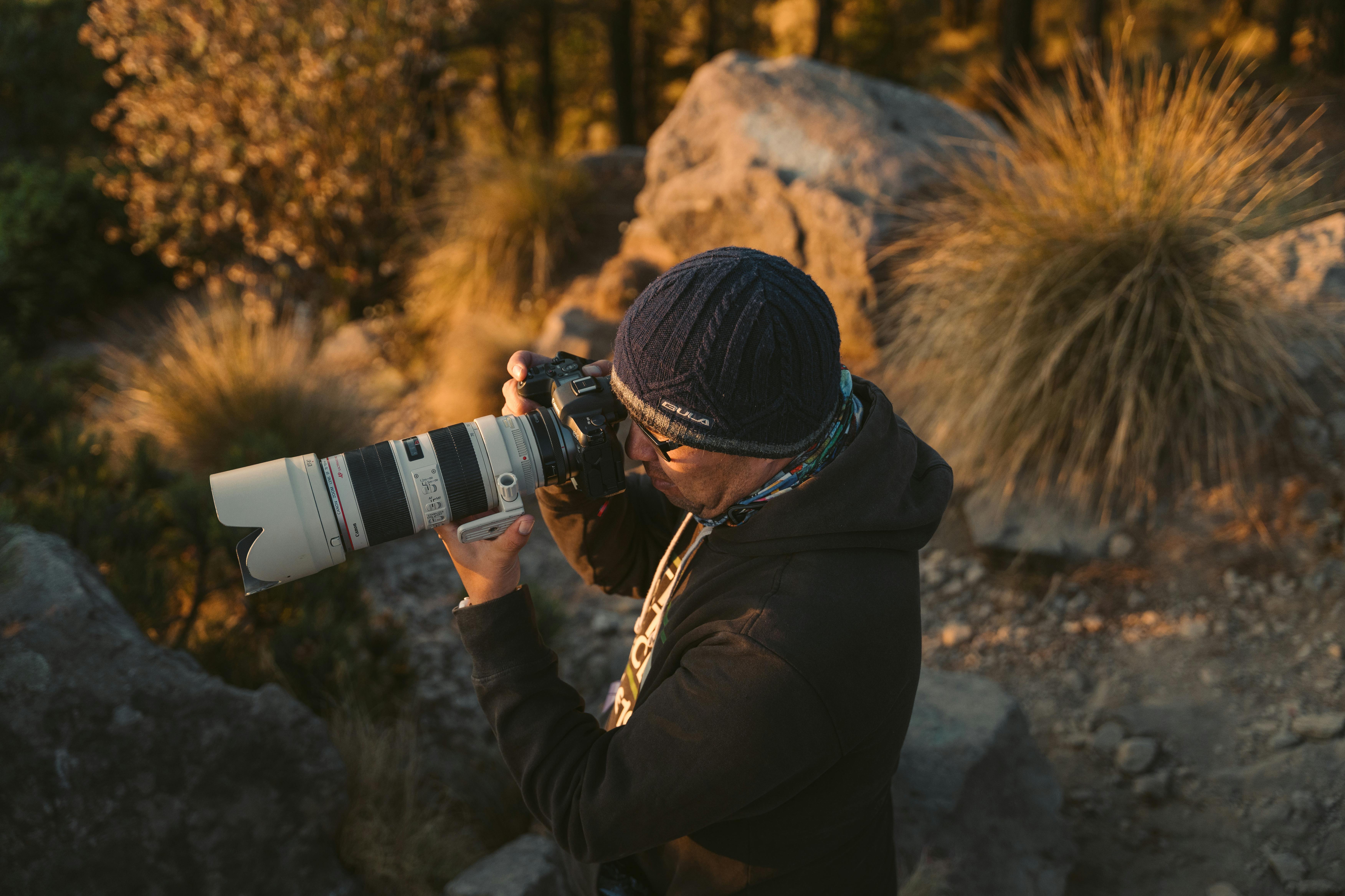 Outdoor shot of a photographer using a telephoto lens camera amidst nature's rocky landscape.