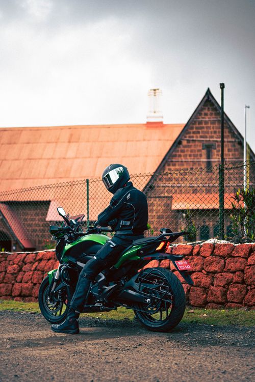 Free A motorcyclist in riding gear poses on a green bike near a rustic brick house outdoors. Stock Photo