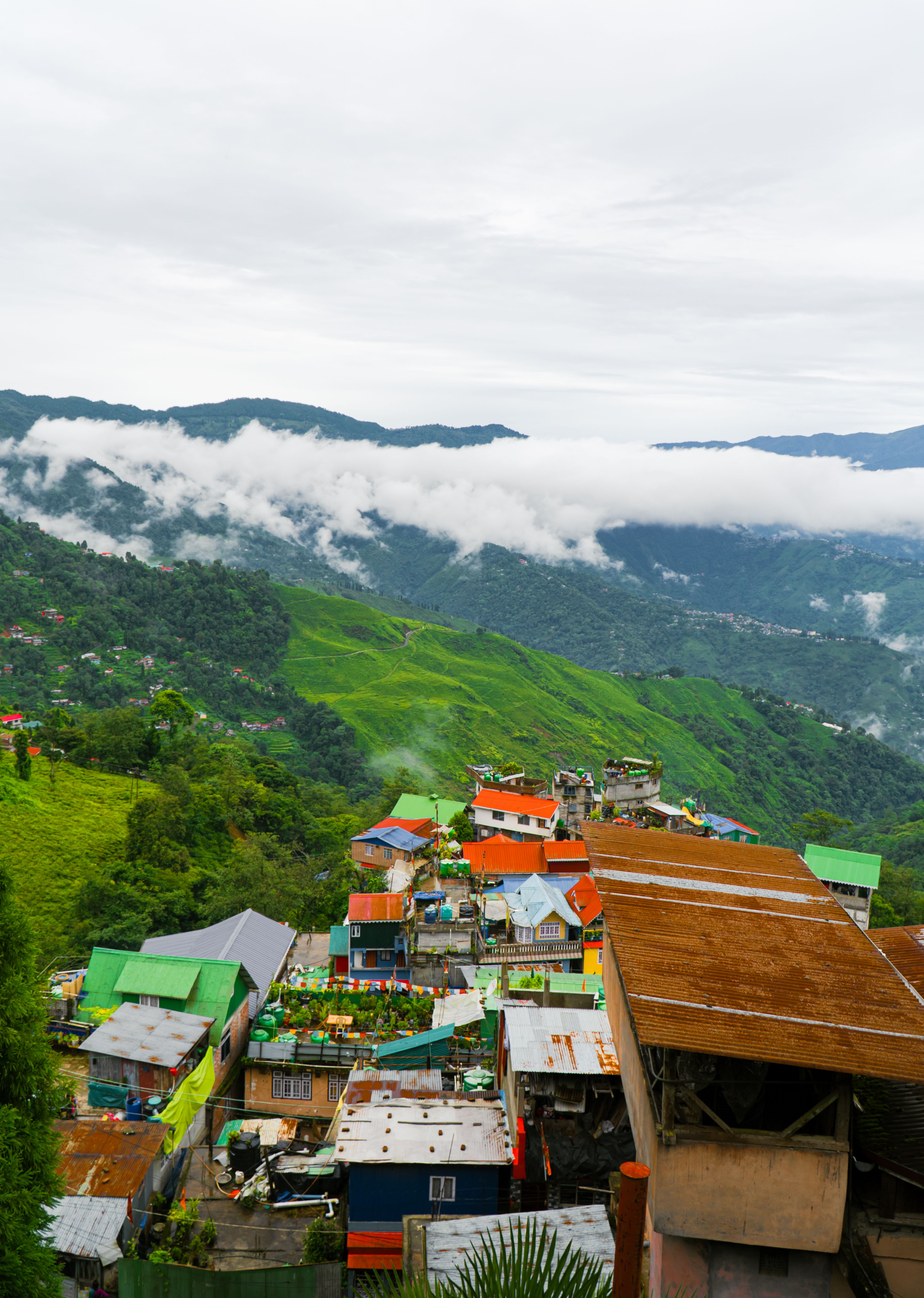 Tejados de colores de Darjeeling bajo laderas verdes empinadas, con una larga franja de nubes sobre las colinas