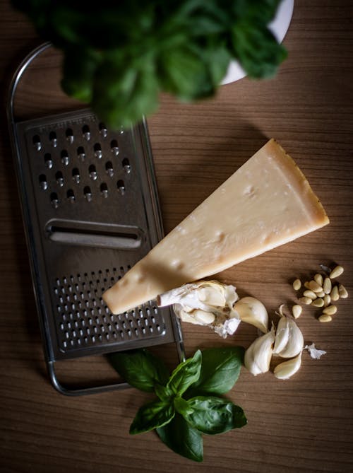 Sliced Cheese Beside Garlic, Basil and Cheese Grater on Table