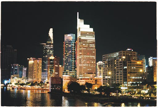 Vibrant night view of Ho Chi Minh City's illuminated skyline with reflections on the water.