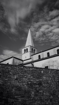 Black and white photo of Poreč bell tower with a stone wall foreground.