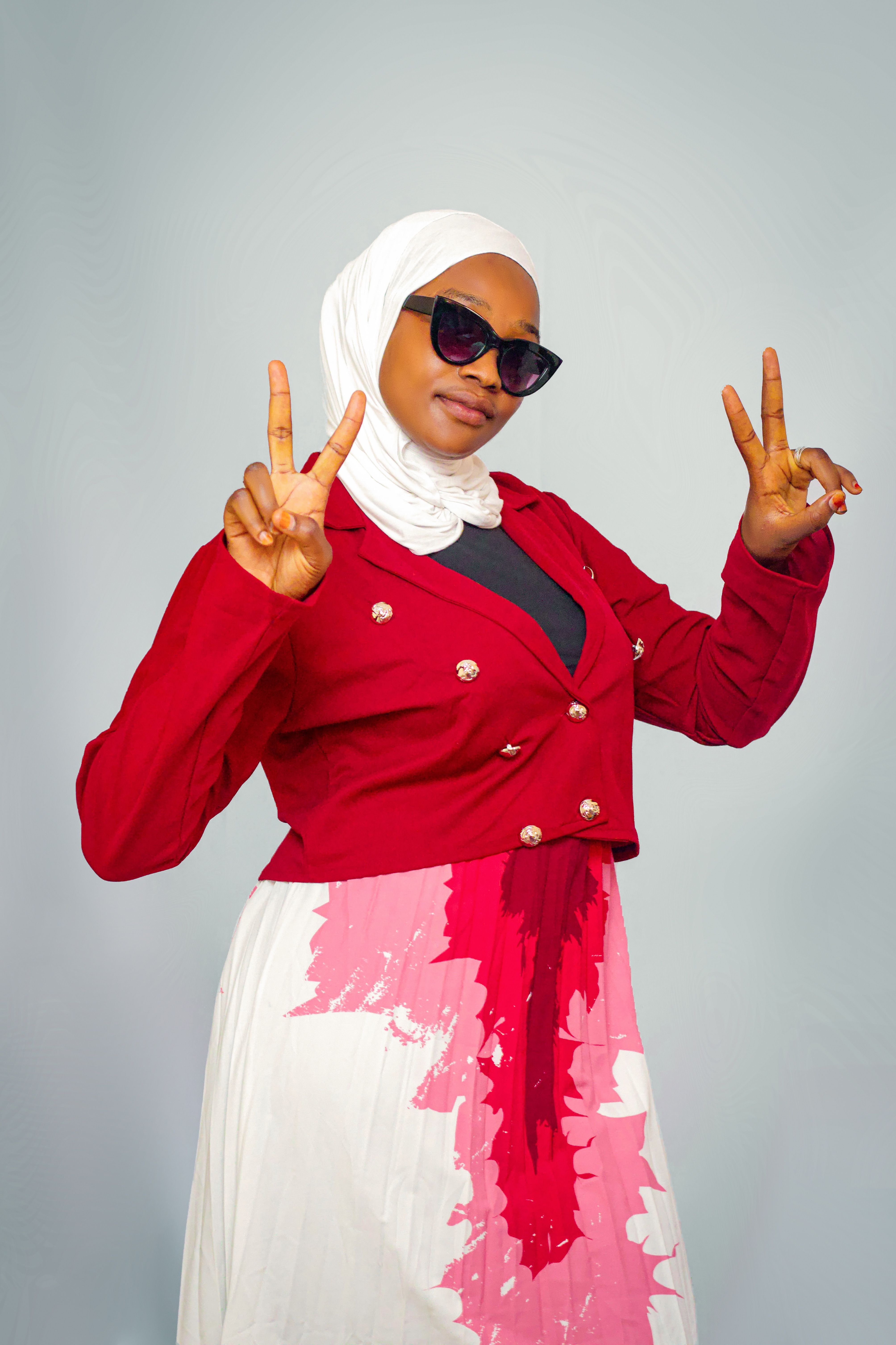 Woman in trendy red outfit and hijab making peace signs indoors.