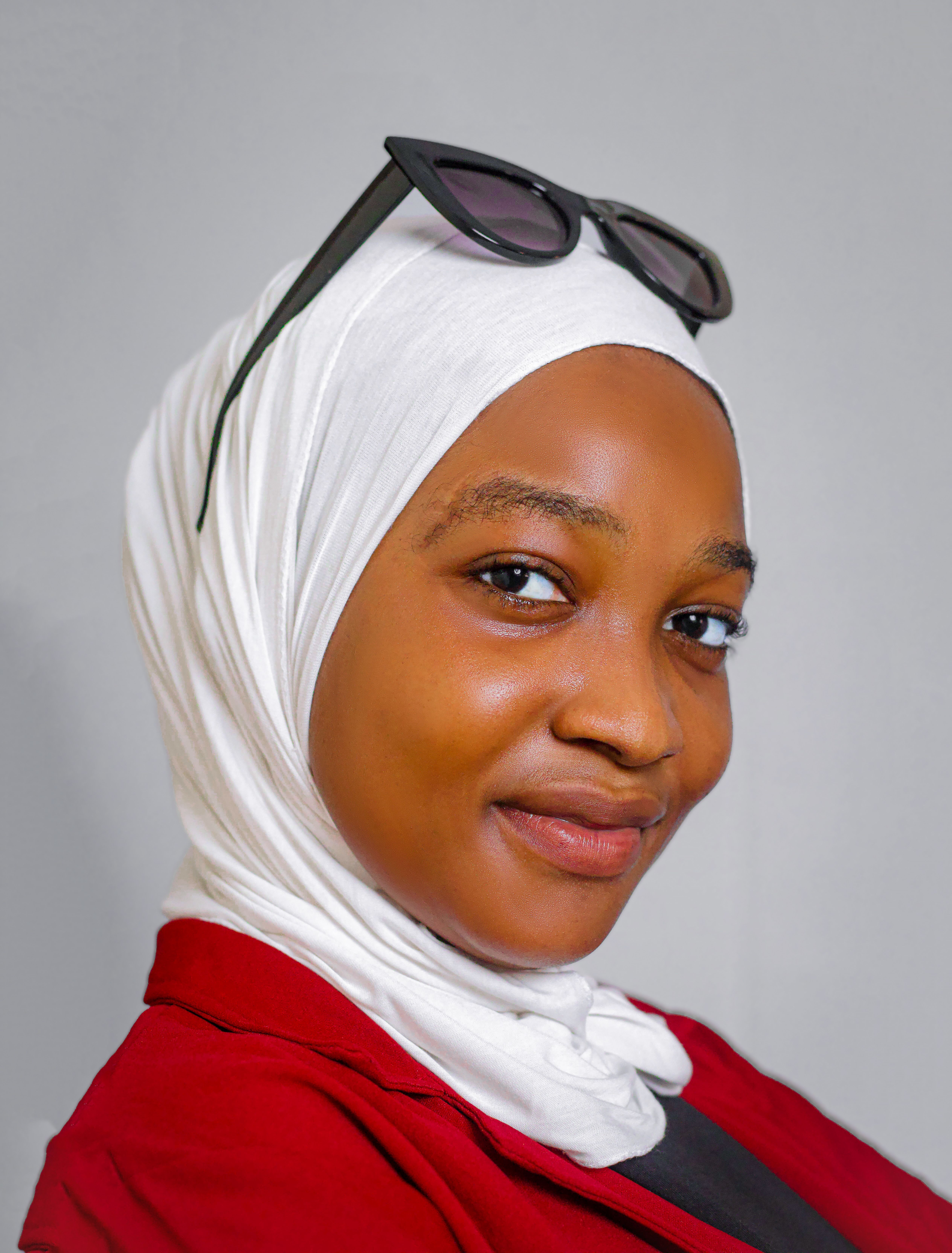 Charming portrait of a young woman wearing a white hijab and sunglasses, smiling confidently.