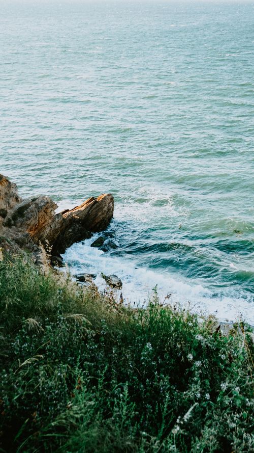Free Breathtaking coastal scene with waves crashing against rocky cliffs and lush greenery. Stock Photo