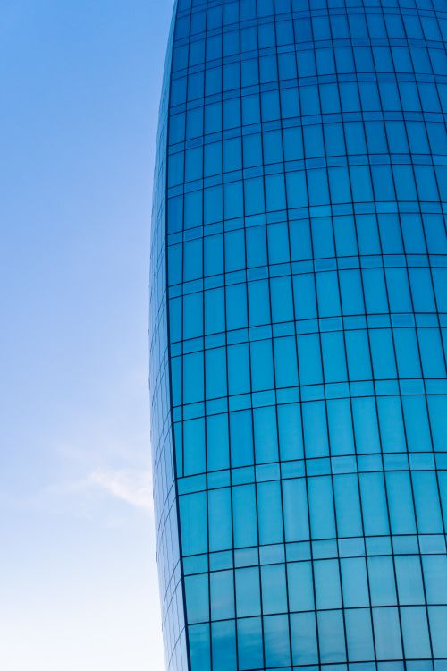 Free A sleek glass skyscraper showing its blue facade against a clear blue sky, reflecting modern architecture. Stock Photo