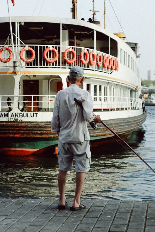 Free A man fishes near a ferry in Istanbul, capturing a blend of city life and leisure. Stock Photo