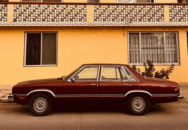 Maroon sedan parked in front of a yellow brick facade — photo by Bien Agusto on Pexels