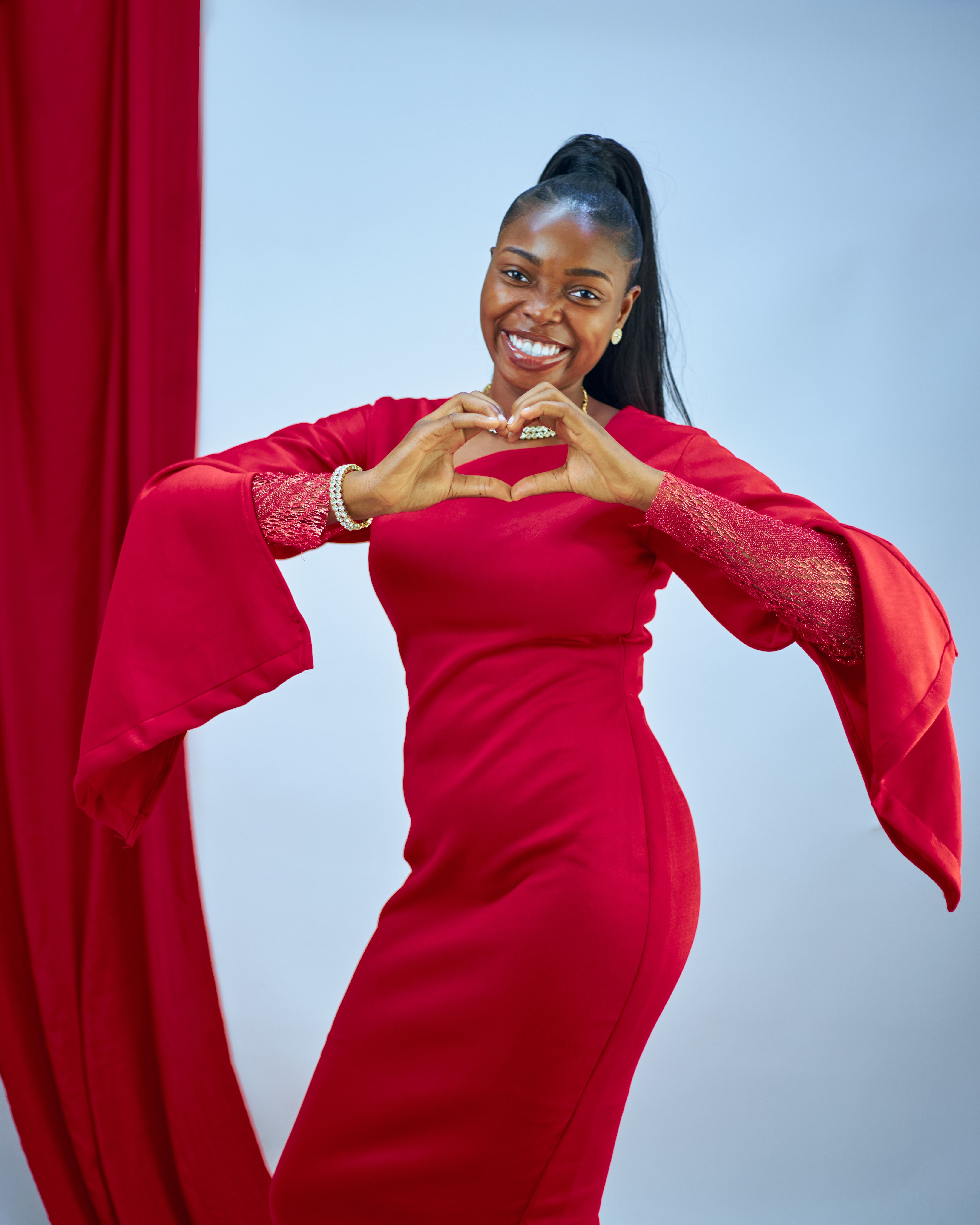 Woman in a red dress making a heart symbol with hands, expressing love and positivity.