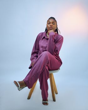 Elegant woman seated in a studio wearing a fashionable purple outfit, exuding confidence.