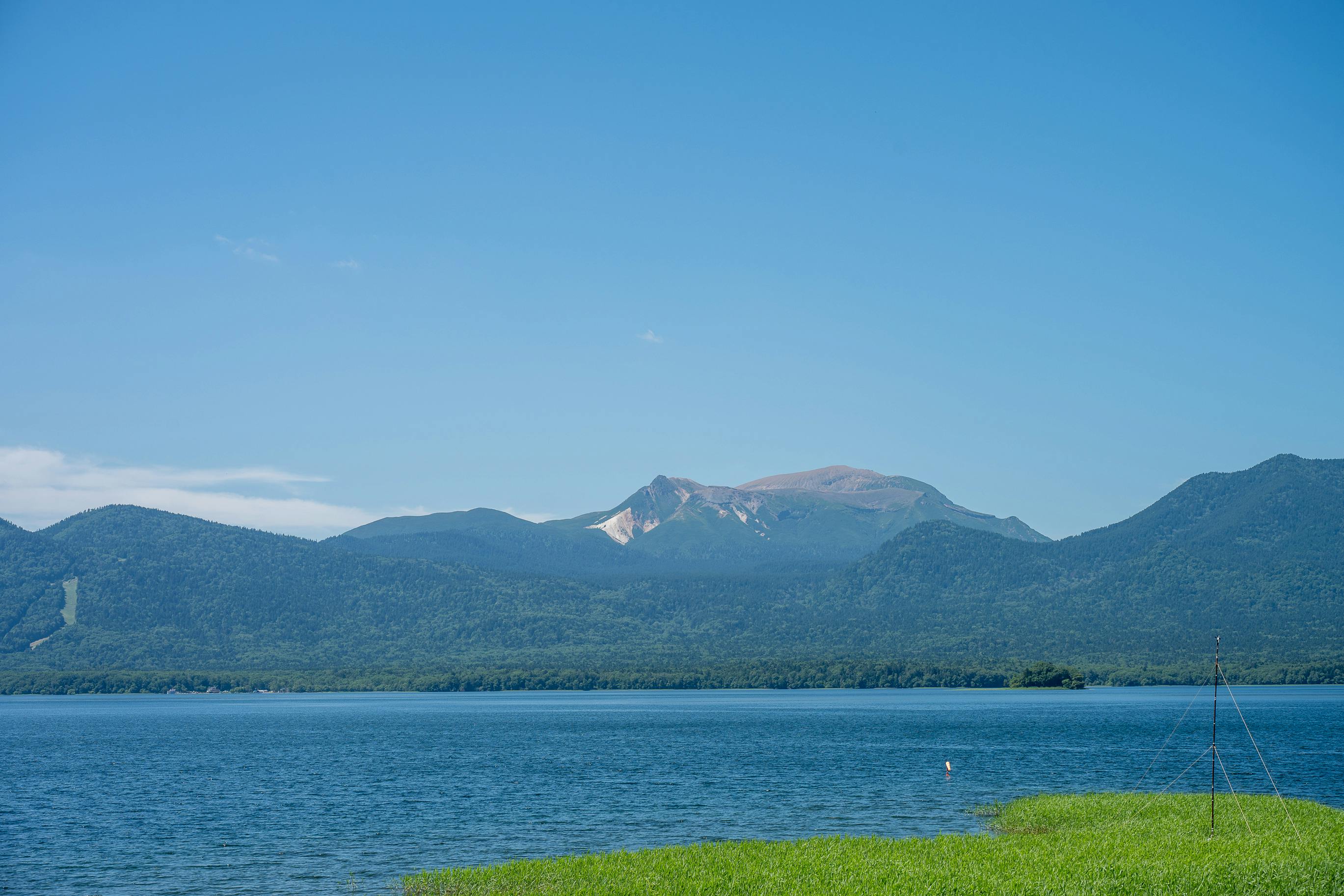 The deep blue waters of Lake Tazawa shimmer beneath golden sunlight, framed by forested mountains in Akita, Japan.