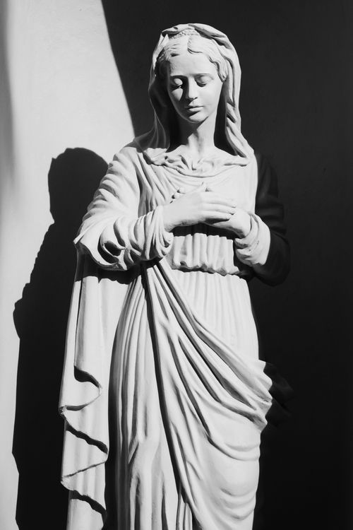 Free Black and white photograph of Virgin Mary sculpture casting a subtle shadow, evoking a sense of serenity. Stock Photo