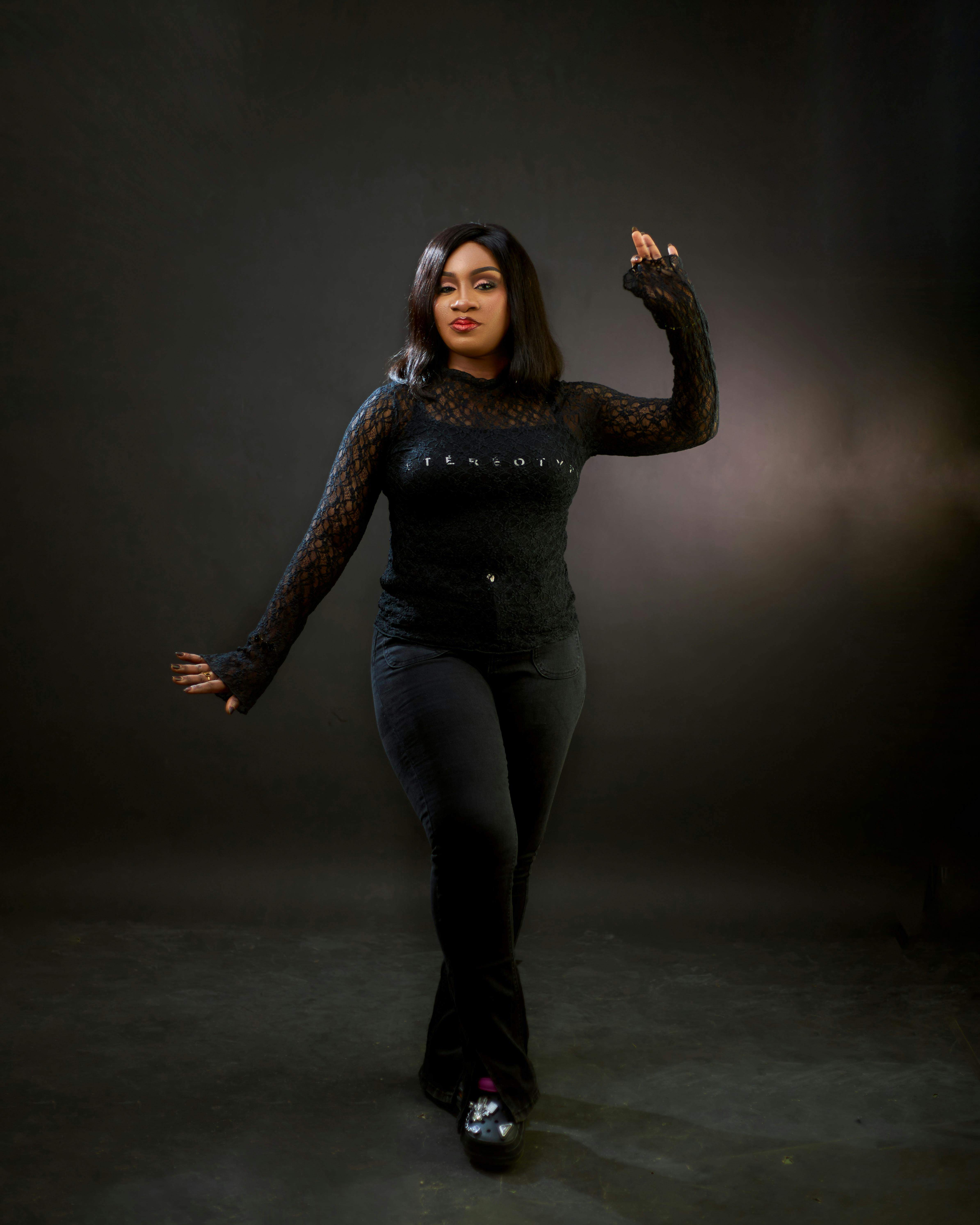 Confident woman standing against a dark background in a stylish black outfit.