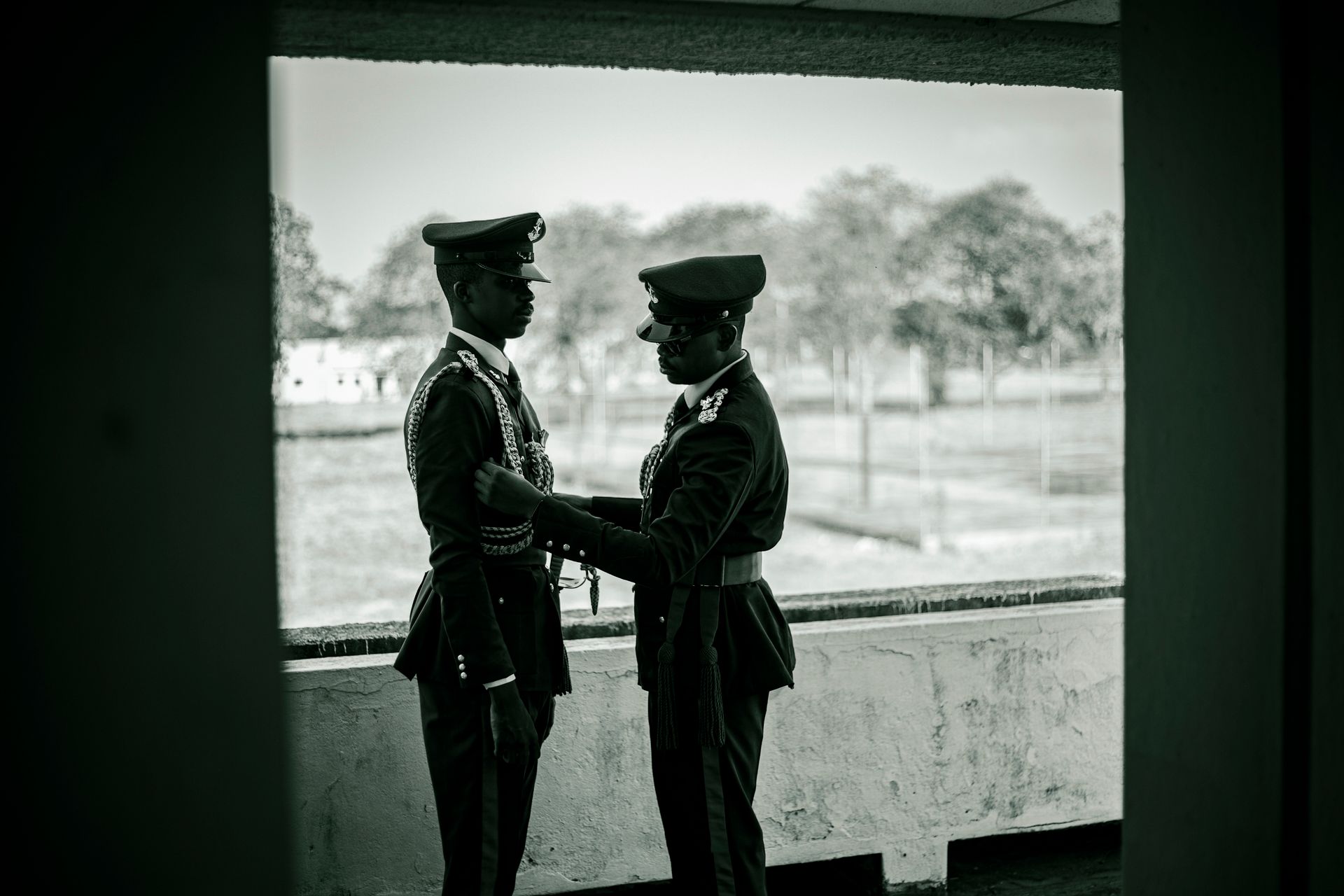 Two soldiers in uniform assisting each other in an outdoor setting. Military camaraderie scene.