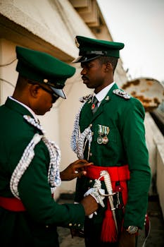Two uniformed guards assisting each other in putting on ceremonial military attire.