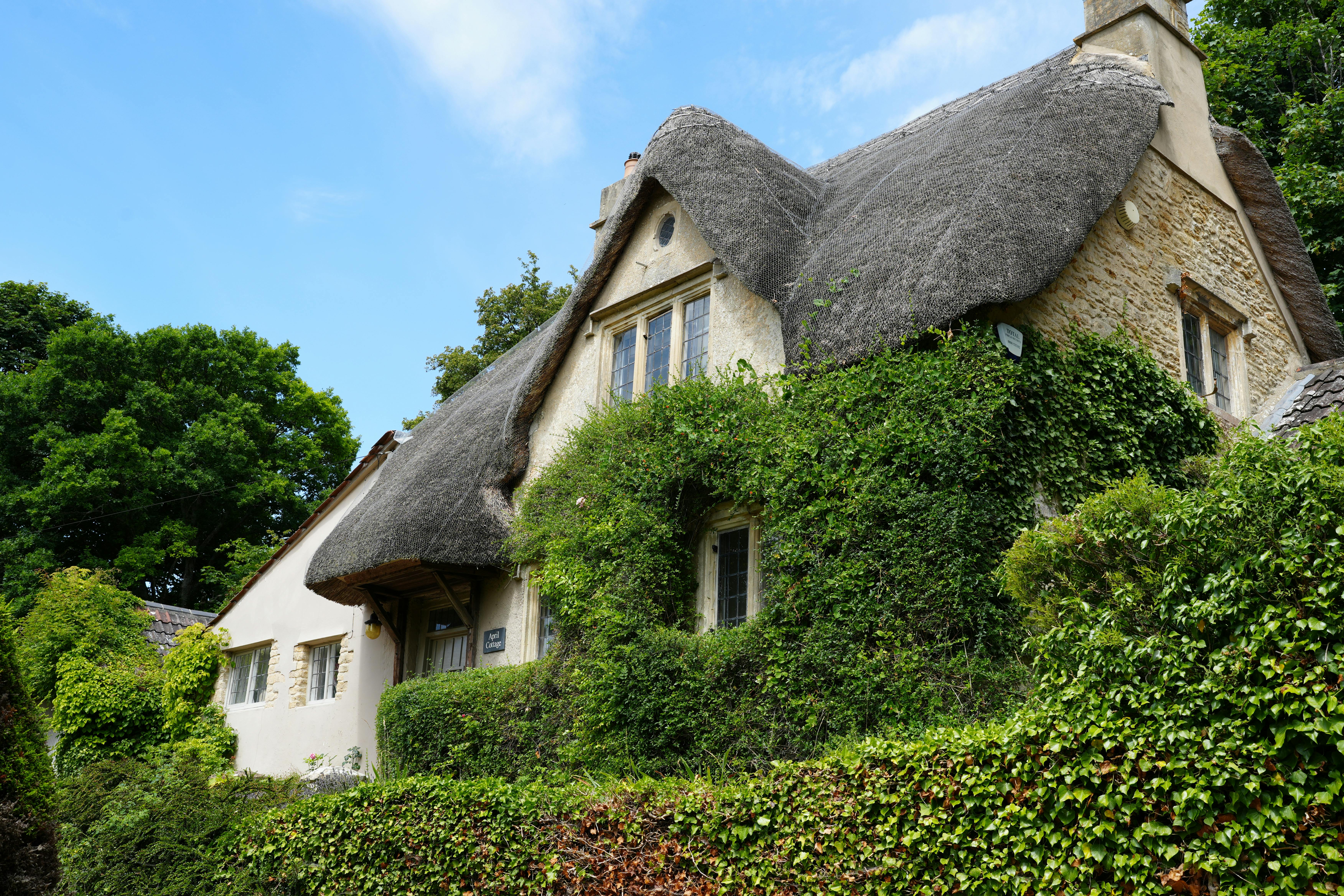Rolling green hills and a classic honey-colored Cotswold stone cottage under a blue sky