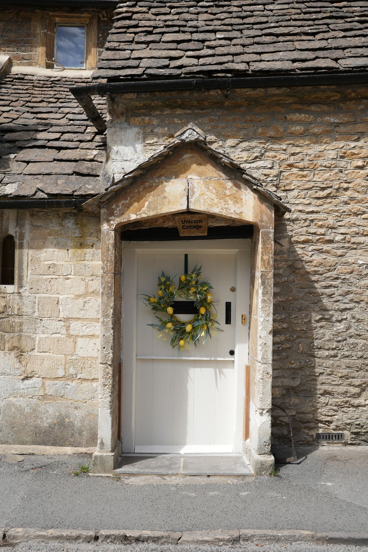 Rustic English stone cottage door adorned with a vibrant lemon wreath, offering a quaint village atmosphere. Stock Photo.