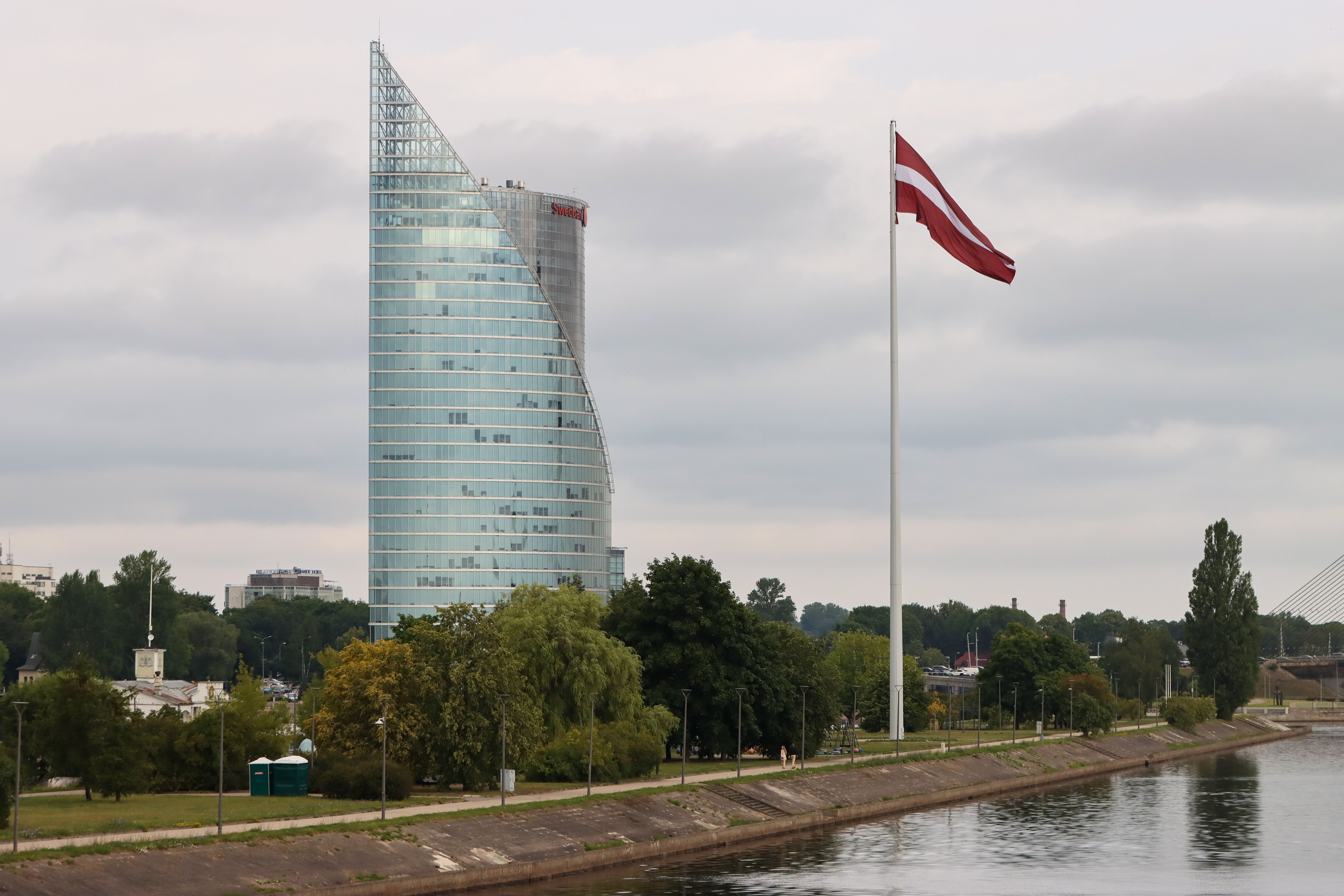 Latvian flag beside a modern glass tower on the Daugava riverfront in Riga
