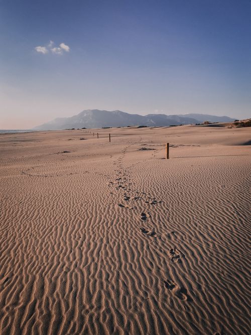 Free Peaceful sand dunes with footprints leading to distant mountains under a clear sky. Stock Photo