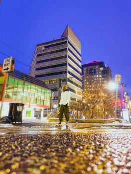 Man standing on a wet street at night in a cityscape with bright lights and buildings.