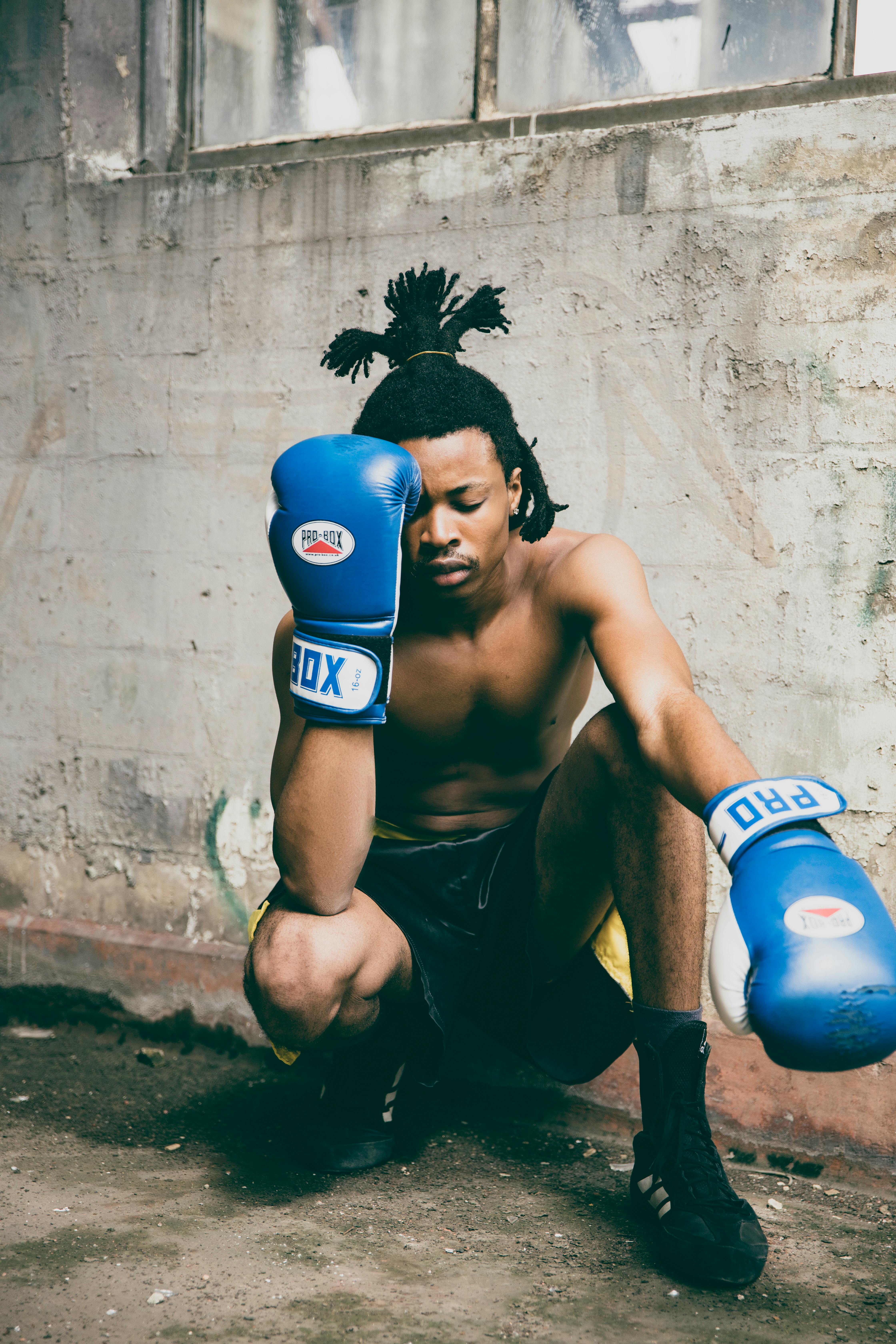 A young boxer with blue gloves kneeling in an industrial setting, reflecting determination.
