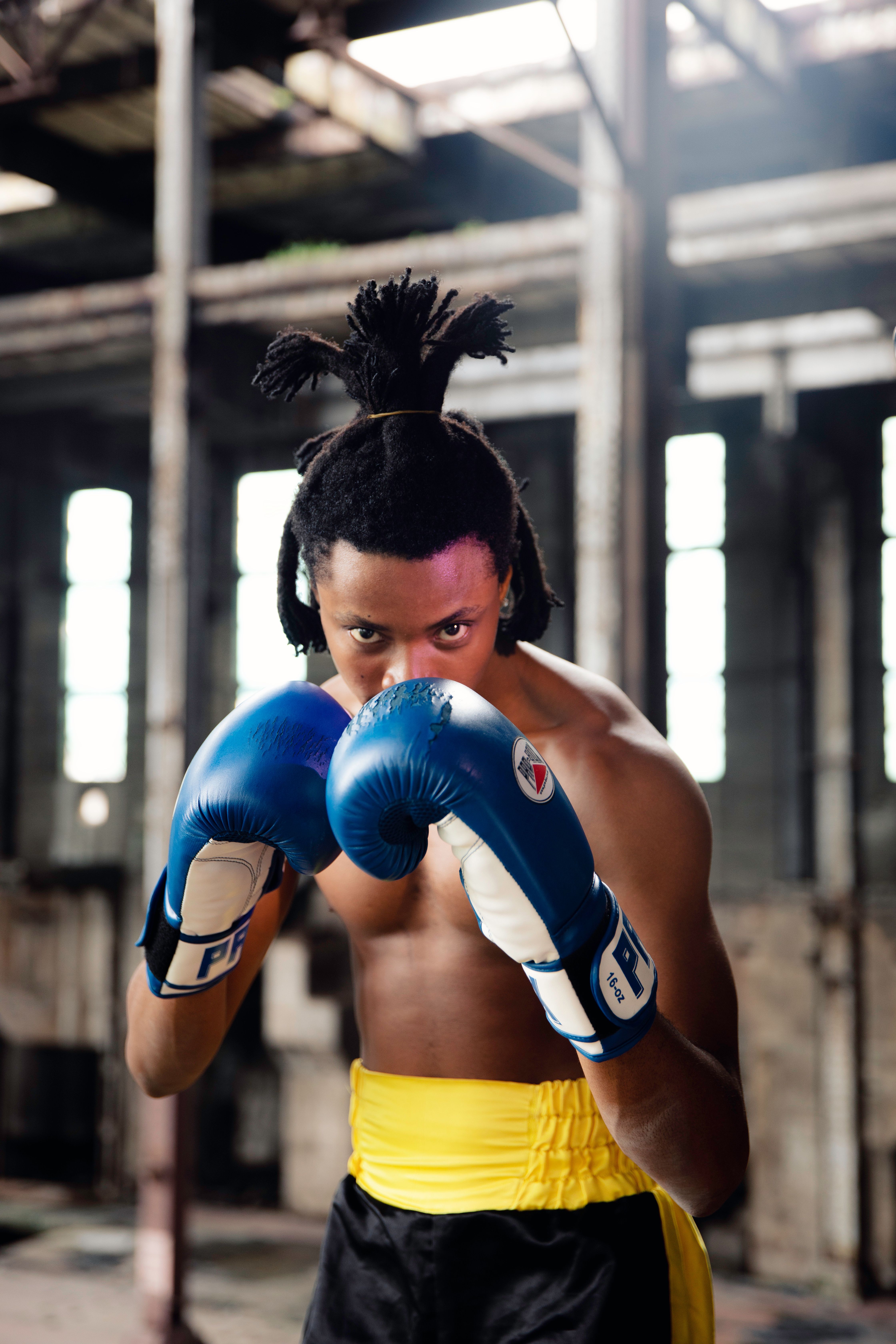 A determined boxer with blue gloves prepares for a fight in an urban gym.